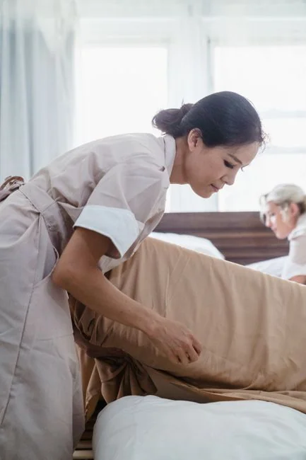 A woman carefully wraps a sofa in protective material while packing boxes in a bright room.